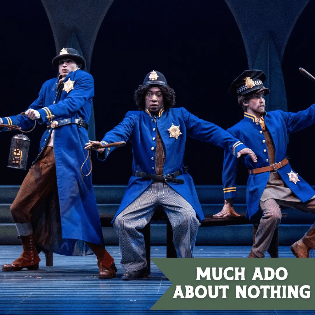 Three actors in blue police uniforms perform a comedic scene from the play 'Much Ado About Nothing' on stage, with a sign displaying the play's title.