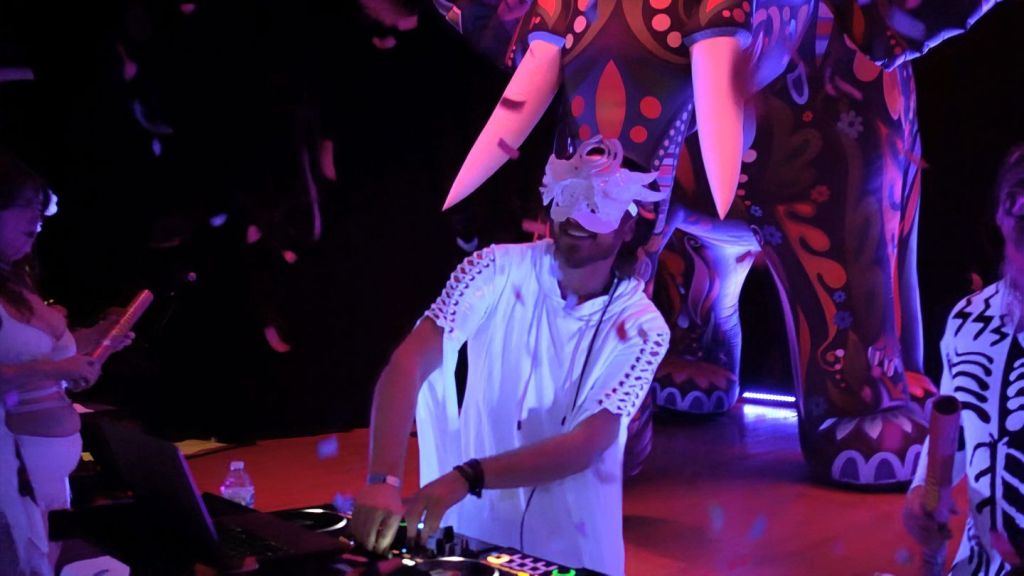 SLC White Party 2026: A Voyage Through Time 7 A DJ performing at the SLC White Party, surrounded by colorful decorations and guests in white attire, creating a celebratory and immersive atmosphere.