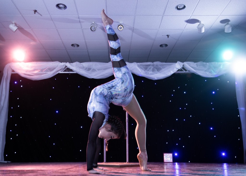 SLC White Party 2026: A Voyage Through Time 6 A performer gracefully executing a handstand on stage, showcasing flexibility and artistry under colorful spotlighting, with a starry backdrop.