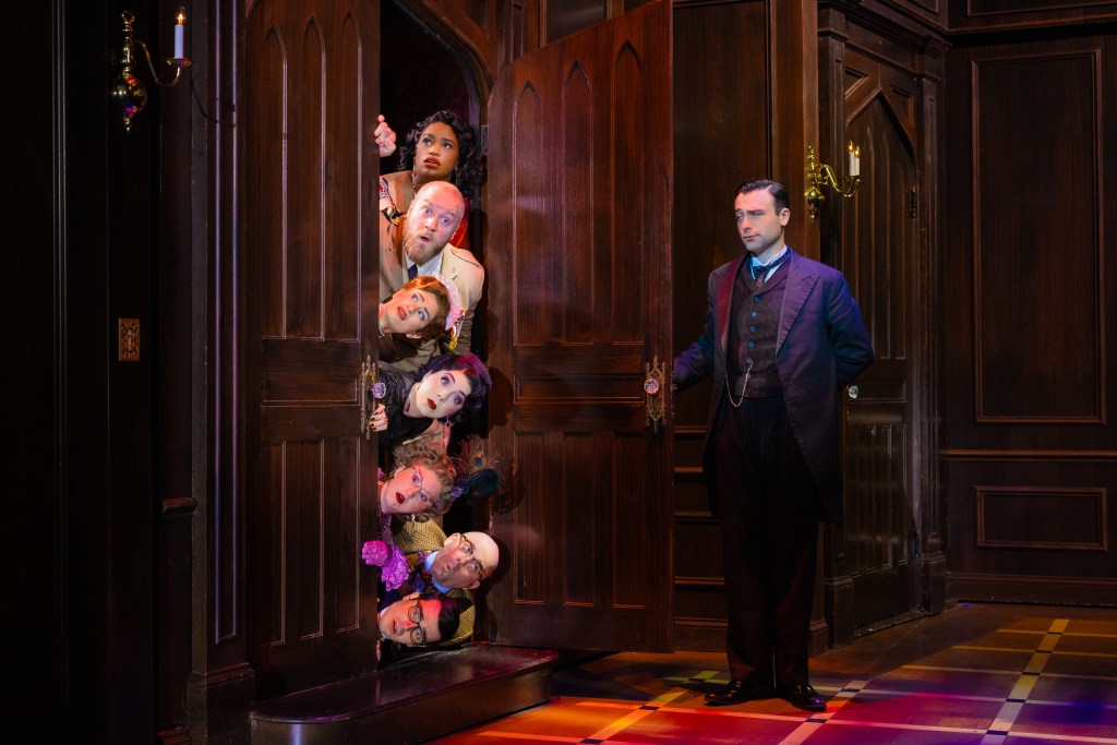 A humorous theatrical scene featuring several characters' heads peeking out from behind a partially open wooden door, with one character dressed in Victorian attire standing beside the door.