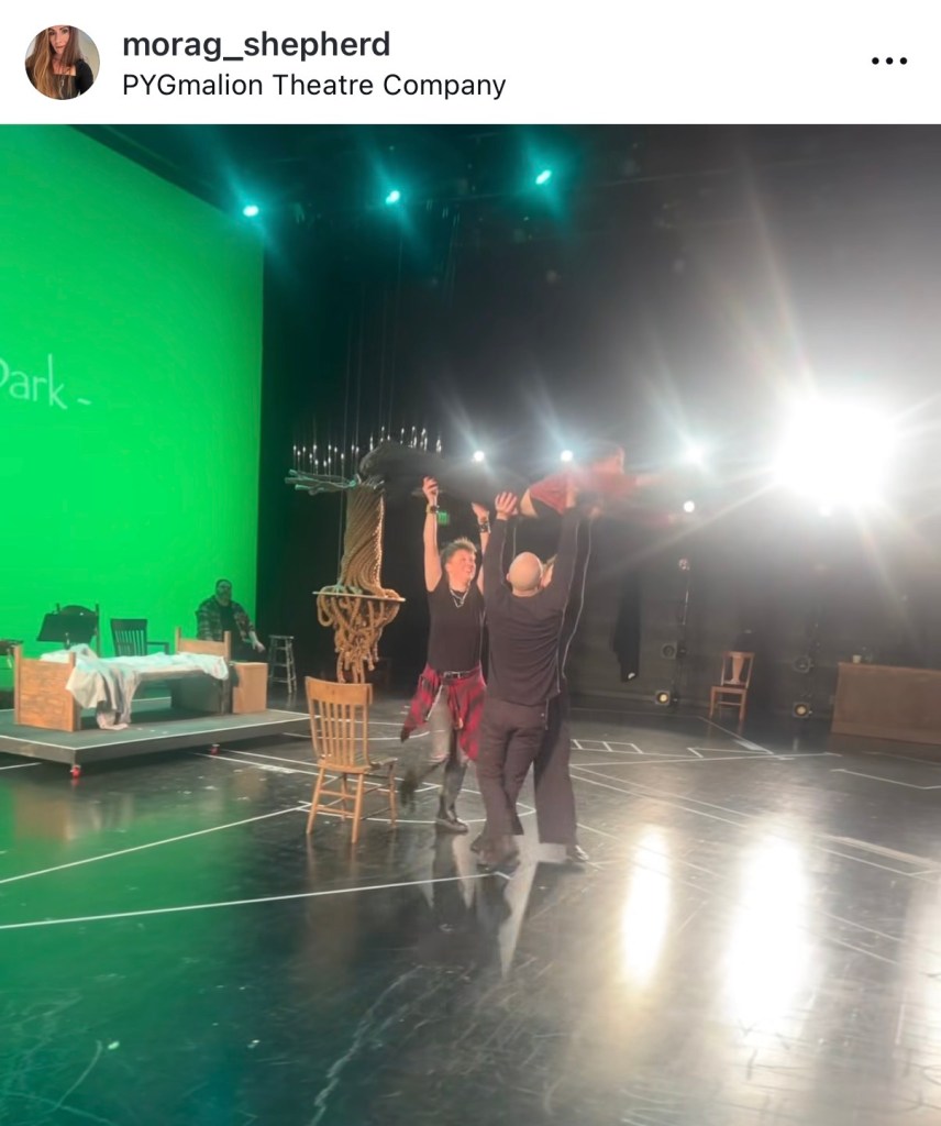 PYG Review: Becky, Nurse of Salem—Returning to the Past to Tell History Differently 6 Actors rehearsing a scene on stage with a green screen backdrop and various props including chairs and a table.