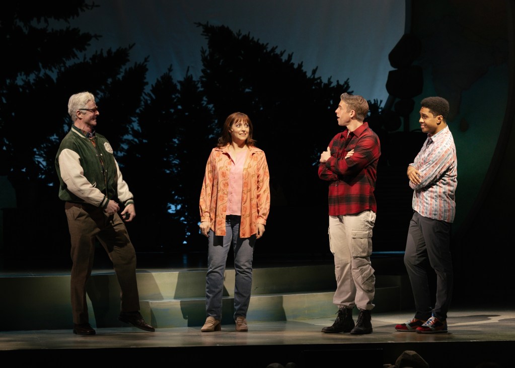 Four performers on stage in a theatrical setting, engaging with each other. The backdrop features silhouettes of trees, creating an outdoor ambiance.