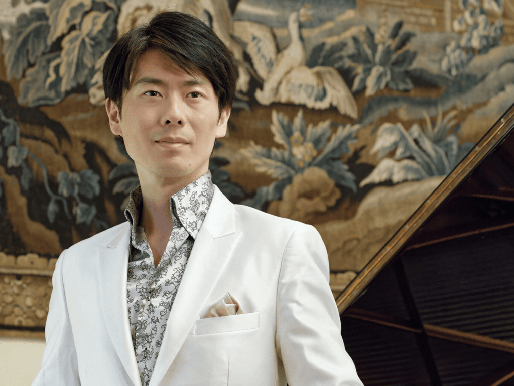 Pilgrimage: A Listener's Guide to Kotaro Fukuma's Liszt Program 3 Kotaro Fukuma poses elegantly in a white suit against a decorative tapestry, embodying the spirit of classical music.