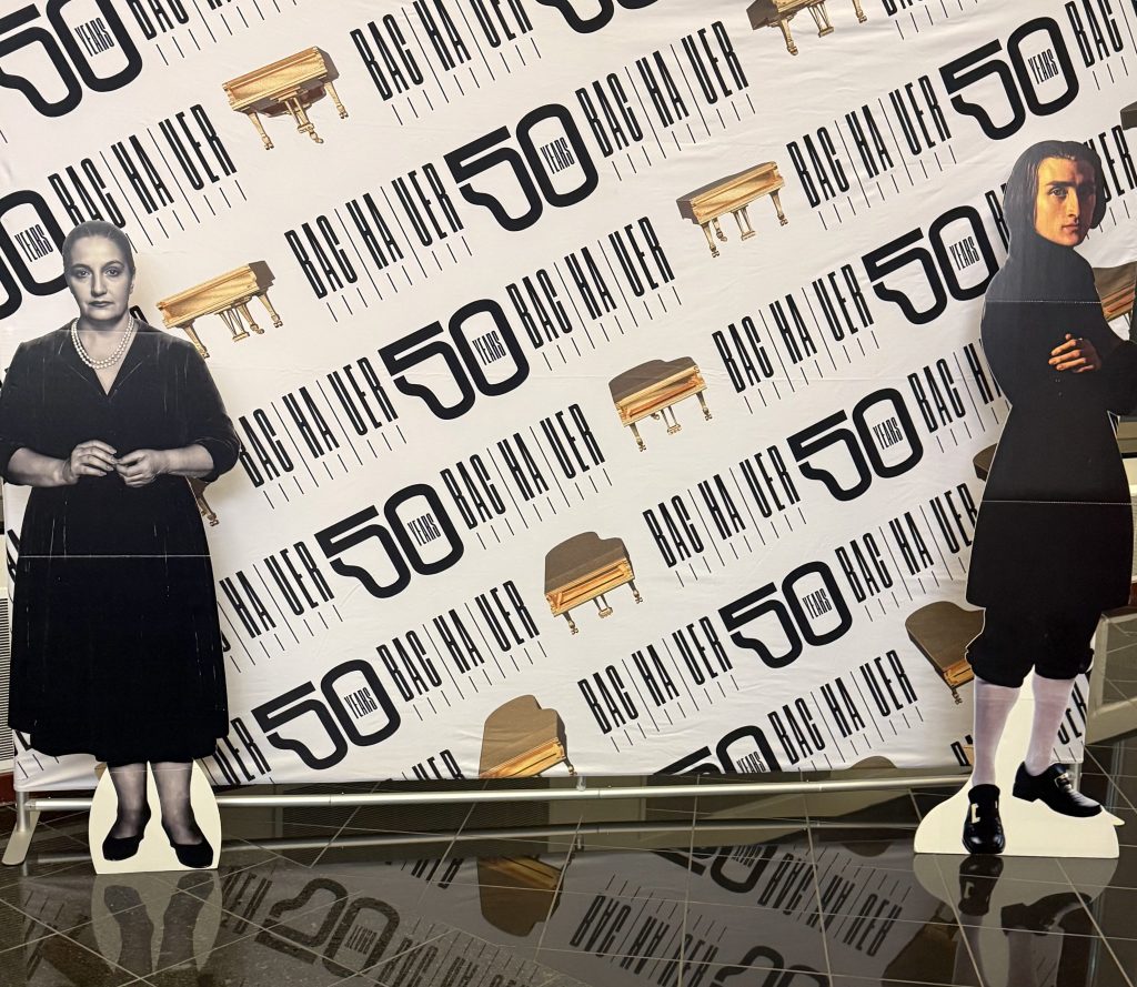 Kotaro Fukuma Opens Bachauer’s 2026–27 Season with Homage to Liszt 4 Two life-sized cardboard cutouts of women in front of a backdrop celebrating a 50-year anniversary, featuring black and white text and images of pianos.