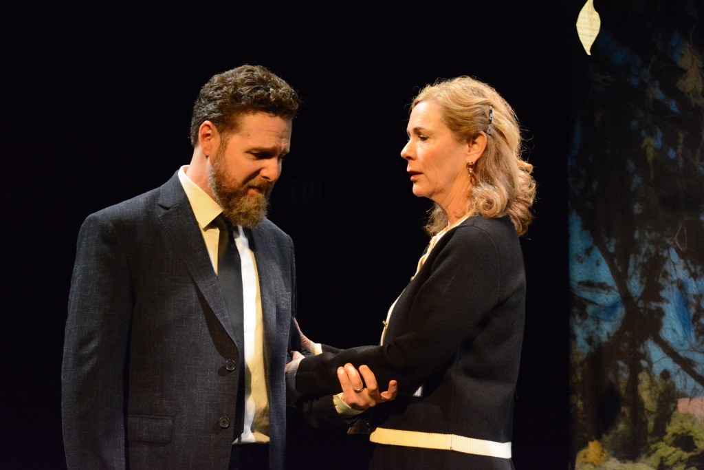 Carol Lynn Pearson's Facing East Returns, Still Asking Utah What Love Costs 4 A dramatic scene featuring a man in a suit and a woman in a black outfit, both displaying emotional expressions. The man looks downcast while the woman appears concerned, set against a dark background.