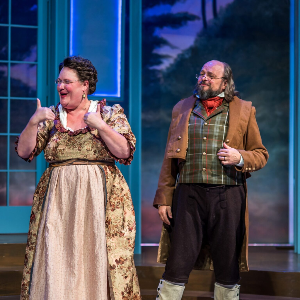 Listening to Mrs. Bennet: Larson’s Pride and Prejudice at The Ruth 4 Two actors perform on stage, with one woman expressing excitement and a man in period costume looking on.